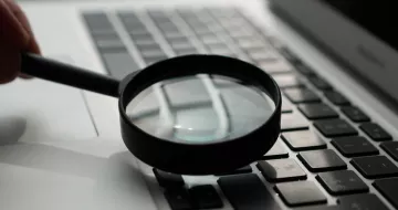 A magnifying glass up against the keyboard of a laptop.