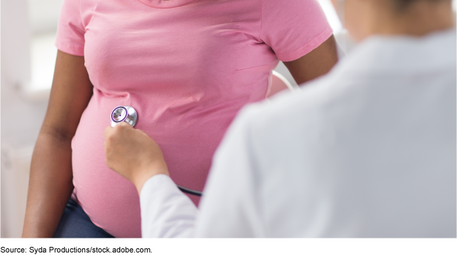 Medical personnel places a stethoscope on the belly of a pregnant woman wearing a pink shirt.