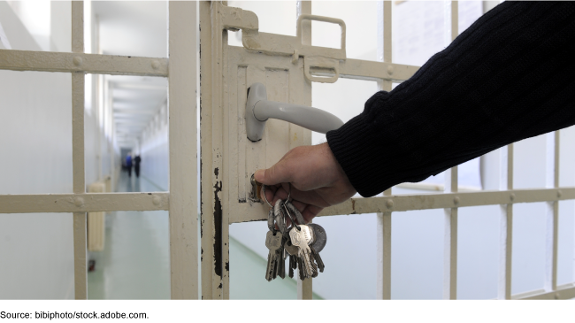 a hand holding keys reaches to unlock a prison door