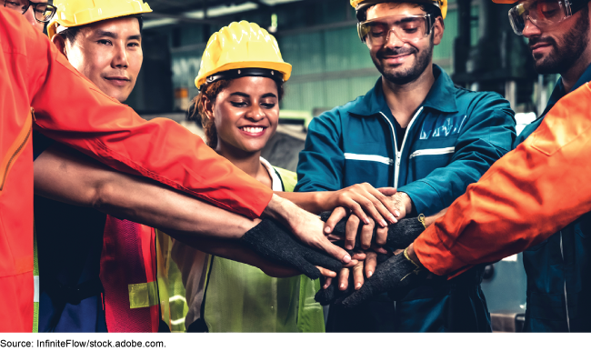 A group of individuals dressed in safety clothing putting their hands together in a huddle.
