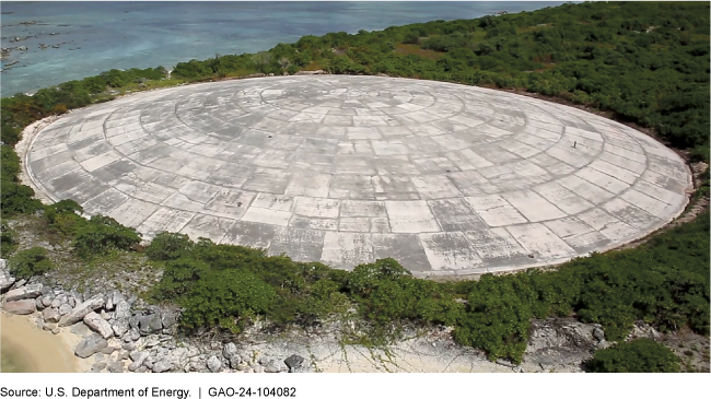 Large dome-shaped concrete structure surrounded by vegetation near a body of water.