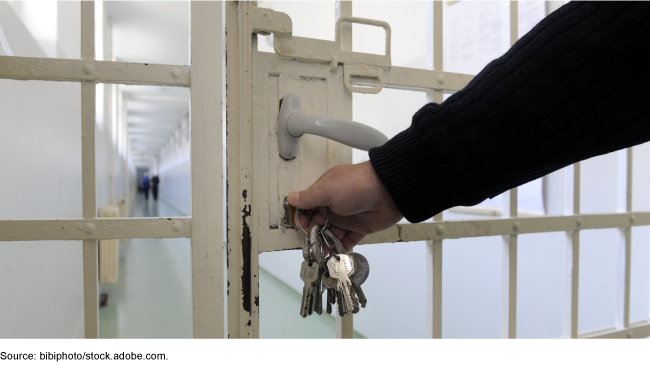 Photo showing a close up of a prison hallway door and a hand with keys unlocking it.