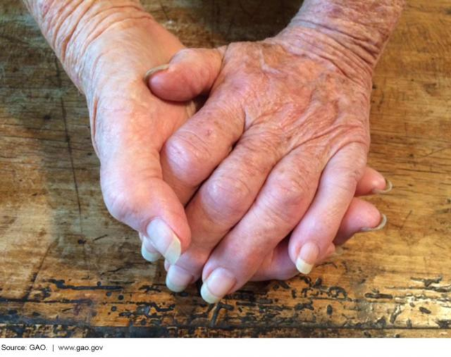 Photo of an older adult's clasped hands on wooden table