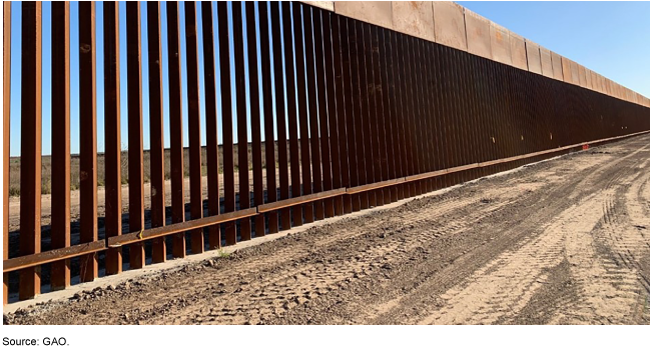 A U.S.-Mexico border barrier next to a dirt road