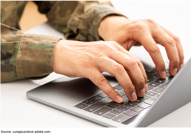 A photo of arms in camouflage sleeves with hands typing on a laptop computer