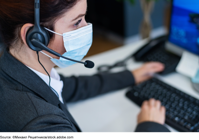 Woman wearing a headset and a mask while seated at a workstation