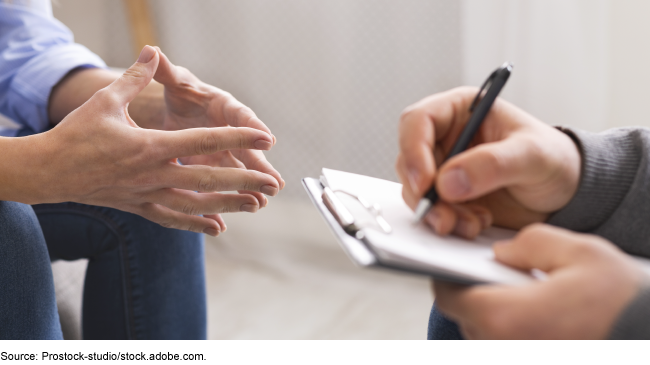 Close up of the hands of two people sitting across from one another while one takes notes