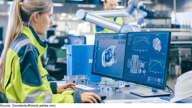 woman in reflective jacket standing in front of a computer in a manufacturing facility