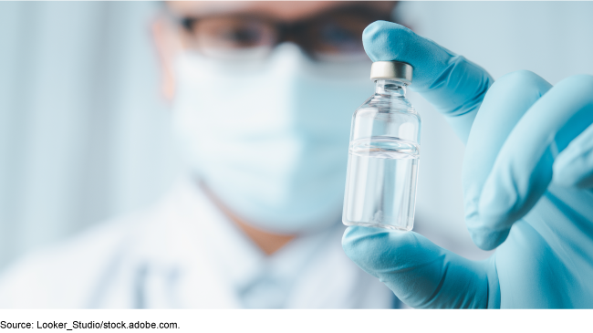 A medical professional wearing blue gloves holding a glass vile filled with clear liquid.