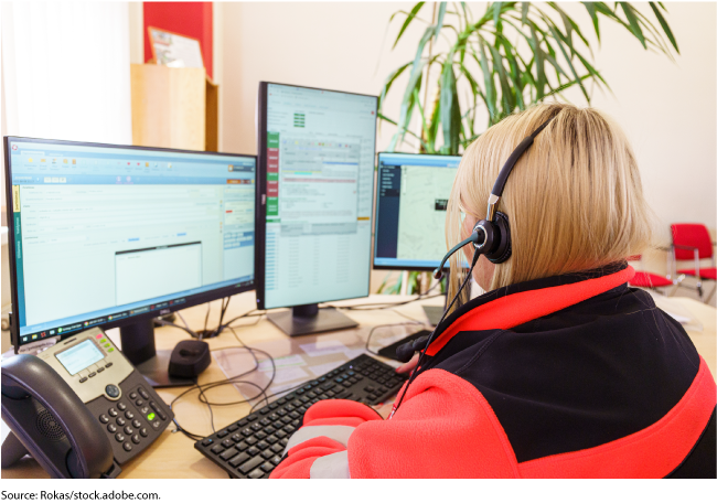 Photo showing a 9-1-1 call center worker at her desk with headset on. 