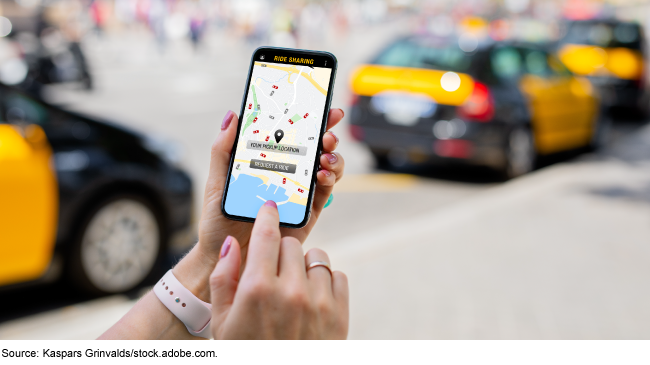 hand holding up a phone displaying a ridesharing app on the screen with taxis in the background