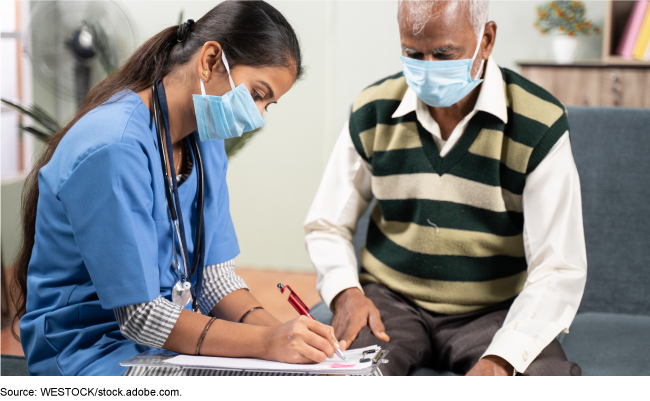 A woman healthcare professional fills out forms with an older man sitting nearby.