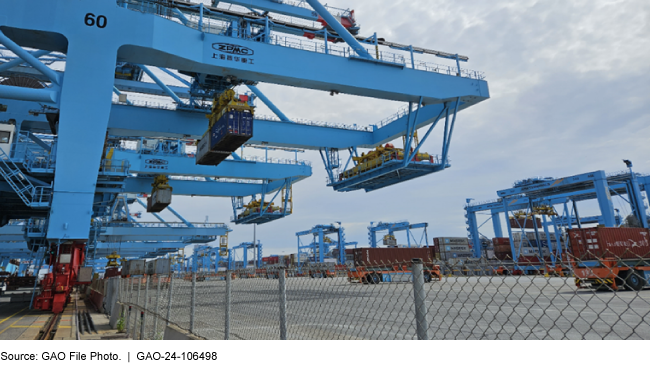 A large crane system with wheels on a track lifts large metal containers into the air