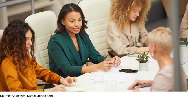 Several women having a conversation while sitting at a conference table.