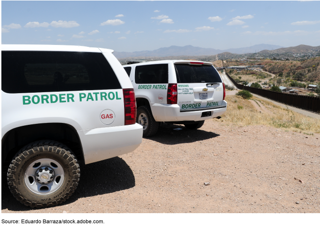 Two white border patrol SUVs parked in the dirt.