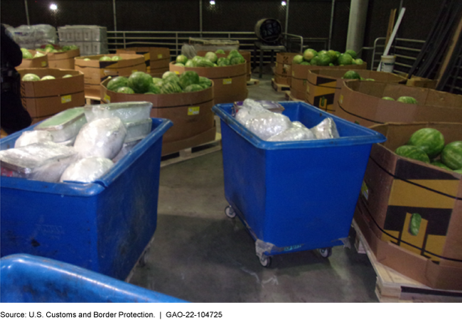 Plastic containers on wheels filled with illegal drugs, surrounded by large containers of watermelons