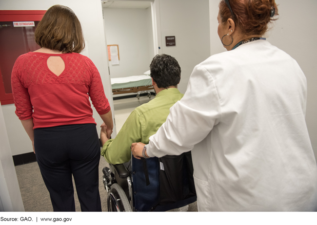 A man being escorted in a medical facility by a loved one and a medical professional