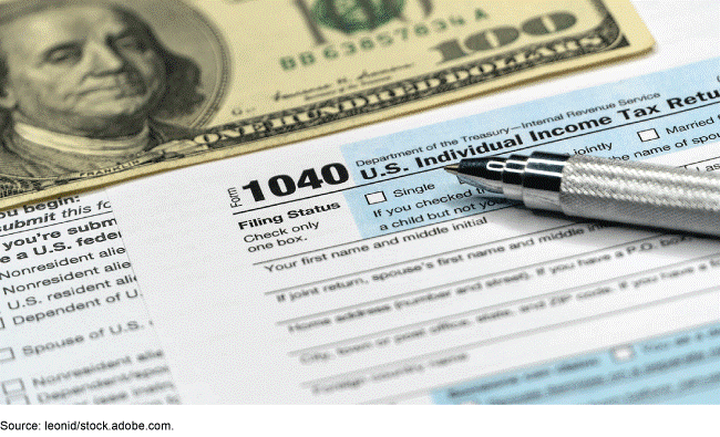 A U.S. 100 dollar bill above a blank federal tax return form with a pen on top of the form.