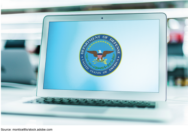 Stock image showing a computer laptop on a desk. The laptop's screen displays the logo for the Department of Defense. 