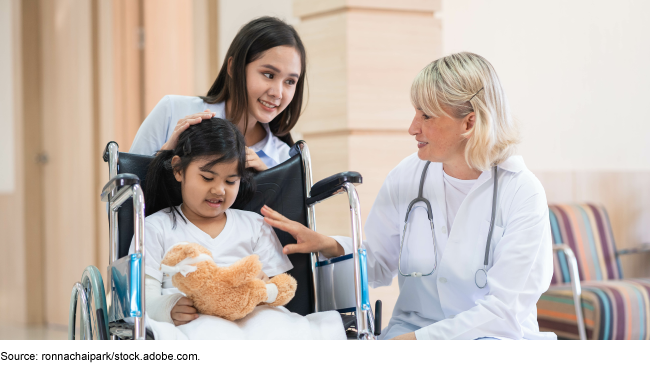 A doctor and mother comforting a child in a wheelchair holding a stuffed animal