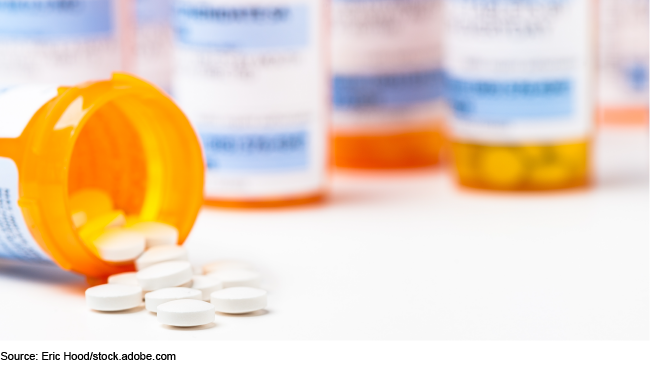 Stock image showing a bunch of orange prescription drug bottles, one of which is on its side with pills spilling out.