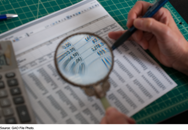 A person using a magnifying glass to look at a financial ledger.