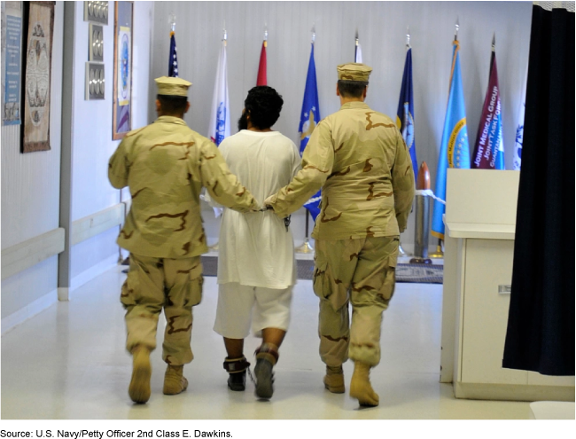 shackled person being led between two uniformed servicemembers
