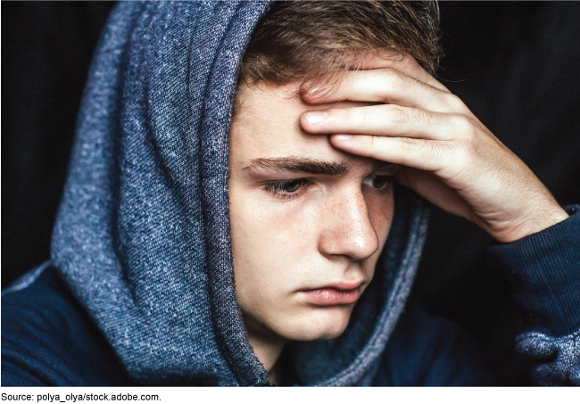 Adolescent wearing a hooded sweatshirt with his hand on his forehead
