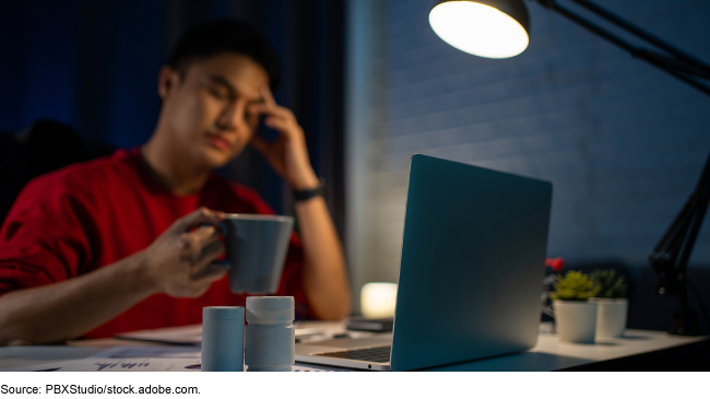 An adult man working at a desk at night looking tired.