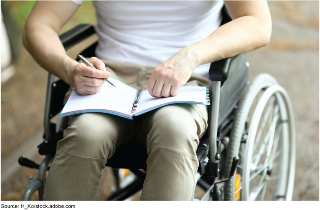 Person in a wheelchair with a notebook and a pen.