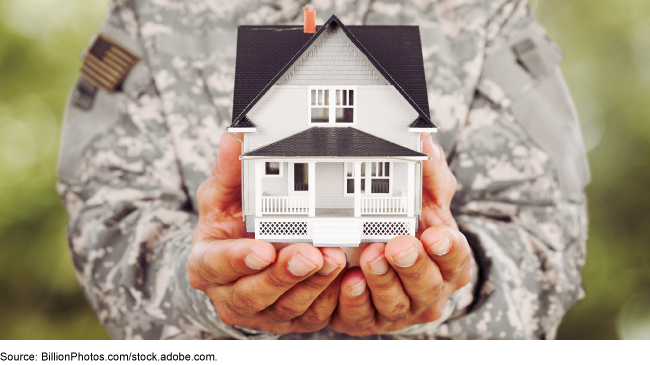 Person in military uniform holding a tiny house. 