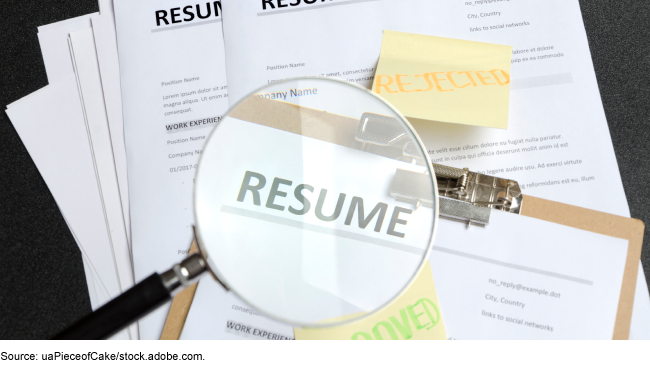 A pile of resumes and a magnifying glass. 