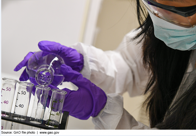 A person wearing laboratory gear pours liquid into vials