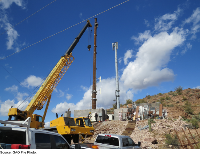 Construction equipment, two towers on a hill, pickup trucks, and workers at a construction site