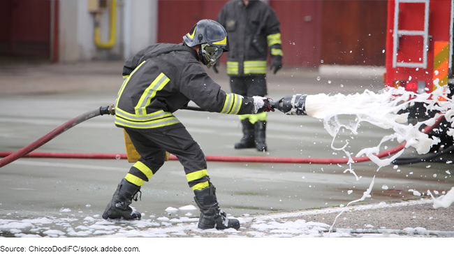 A firefighter spraying a white foam from a hose