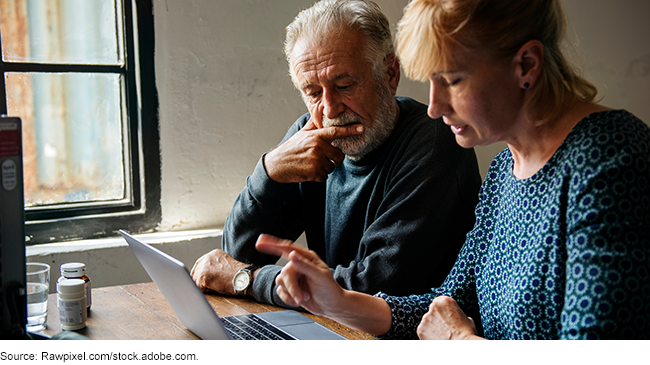 A picture of an elderly individual being helped by someone while they both work on a laptop together.