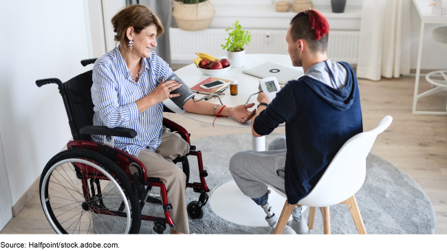 Two individuals with limb replacements sitting at a table taking blood pressure