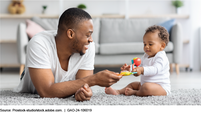 An image of a parent and infant child playing on the floor, sharing a toy together. 