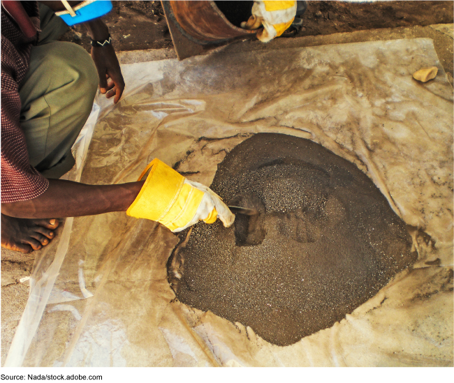 A person kneeling beside a pile of finely ground coltan ore.