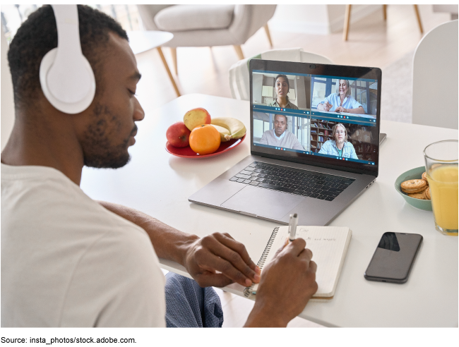 A man sitting at his computer on a zoom call taking notes