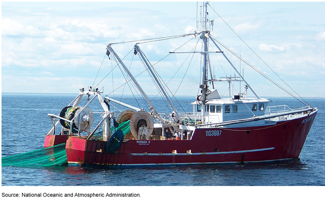 A small, red commercial fishing boat pulls a green fish net in the ocean.