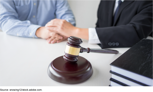 A gavel on a table with the hands of two people in the background.