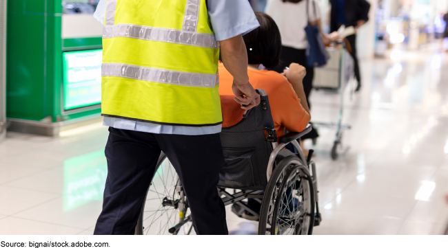 A worker helping a person in a wheelchair through an airport