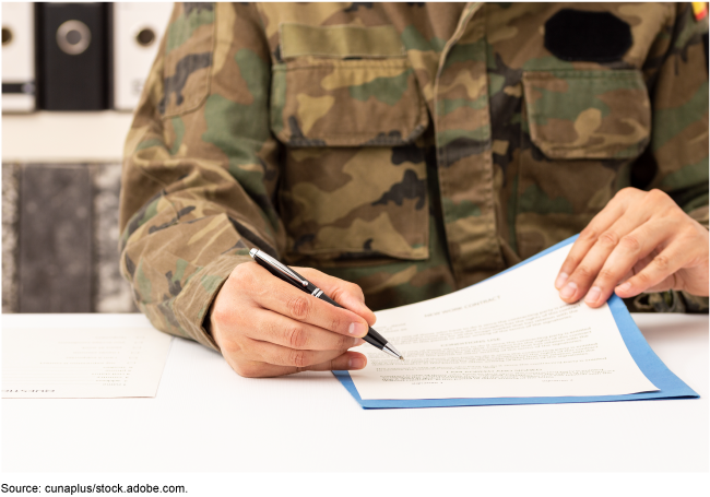 Photo of a person in military fatigues reading over and signing a document