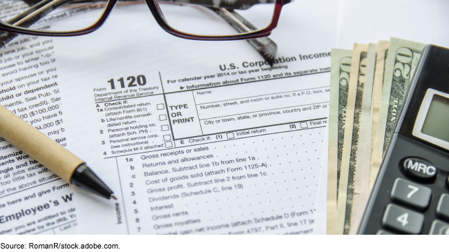 An image of an income tax form with a pen, glasses, calculator, and money sitting on top of it