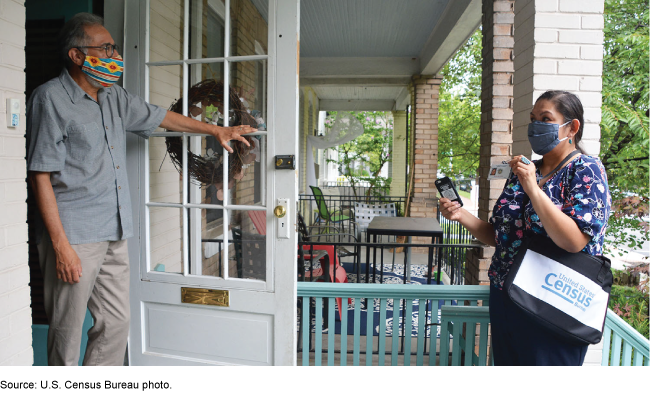 Census worker standing on a porch talking to a person standing in the doorway of their home.