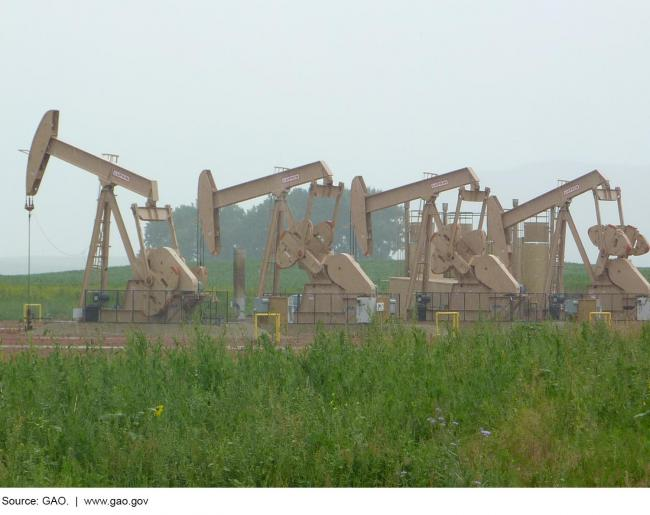 Picture of four oil pump jacks and oil storage tanks.