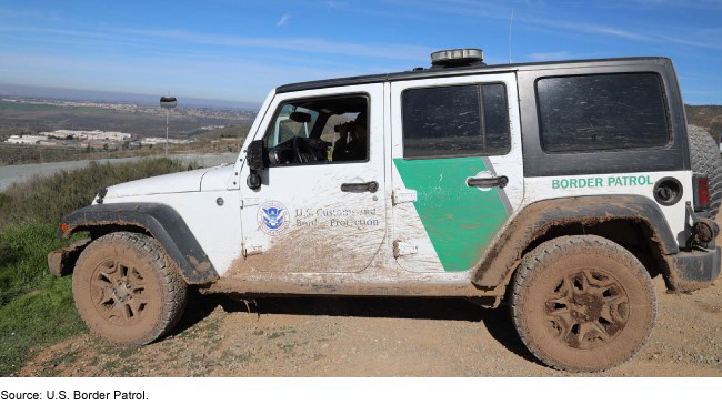 A Border Patrol vehicle covered in mud on top of a hill on a clear day.