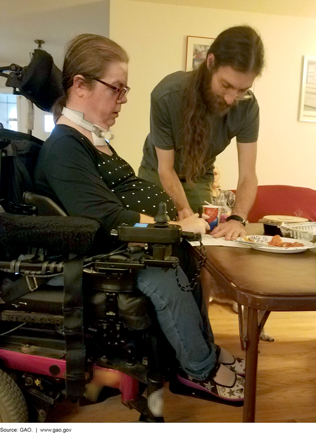 Photo of a woman in a wheelchair and a man at a table.