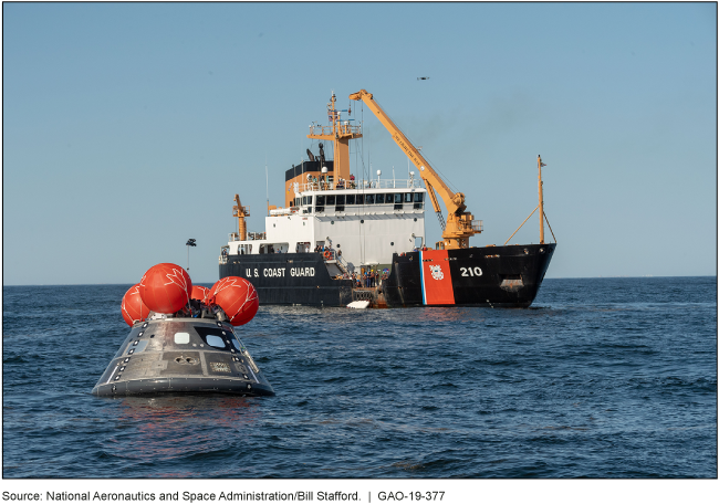 Orion crew module test model floating in the Gulf of Mexico with a Coast Guard boat.